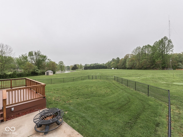 view of yard with an outdoor fire pit, a view of rural / pastoral area, a storage shed, a wooden deck, and an outbuilding