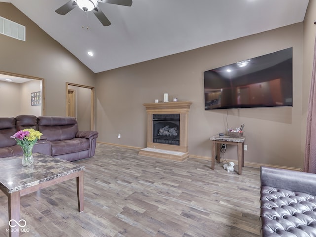 living room featuring a ceiling fan, wood finished floors, a fireplace with raised hearth, baseboards, and high vaulted ceiling