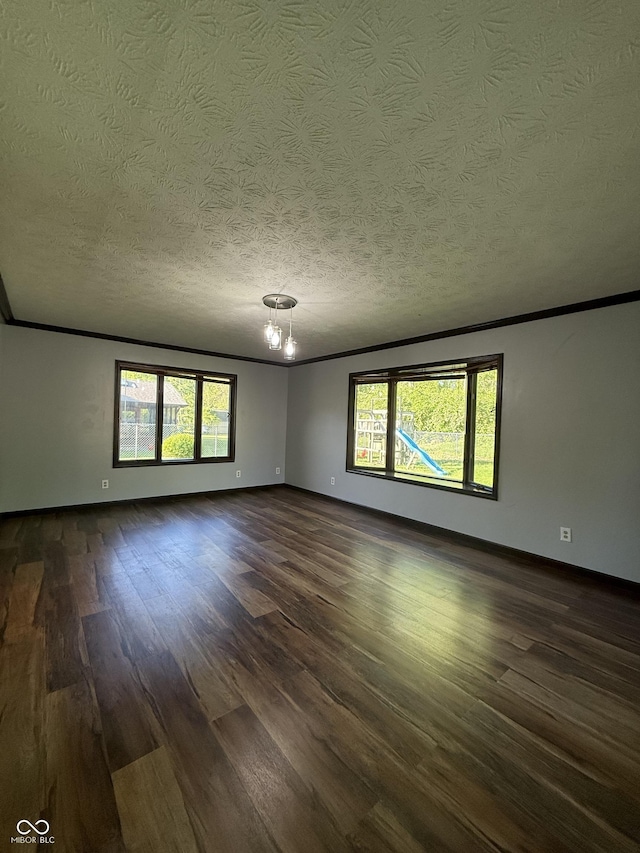spare room with dark wood finished floors, healthy amount of natural light, a textured ceiling, a chandelier, and baseboards