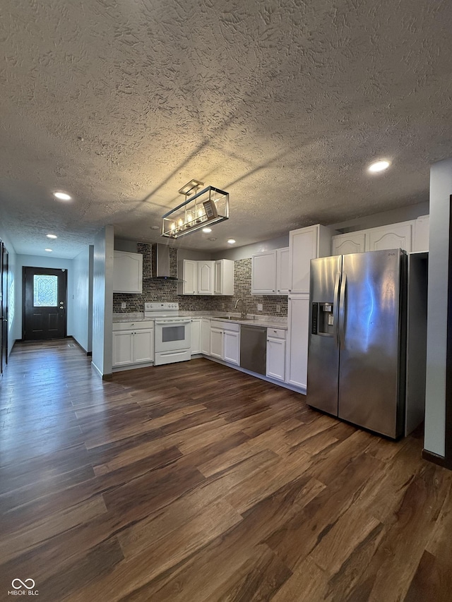 kitchen with appliances with stainless steel finishes, wall chimney range hood, a textured ceiling, white cabinetry, and dark wood-type flooring