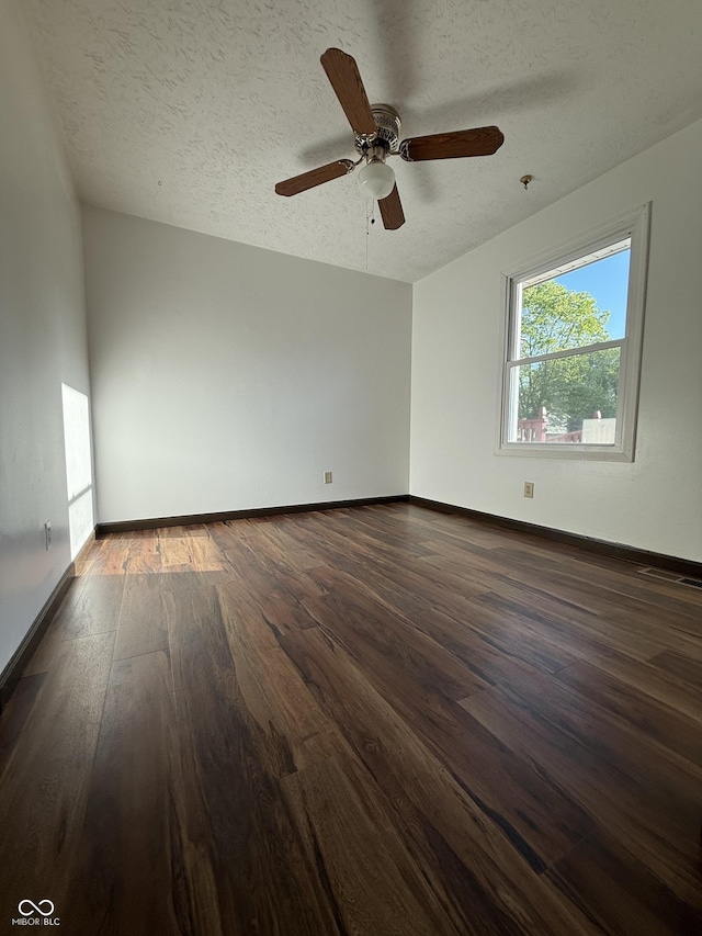 empty room featuring dark wood finished floors, ceiling fan, a textured ceiling, and baseboards