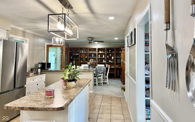 kitchen featuring freestanding refrigerator, a kitchen island, ceiling fan, a textured ceiling, and white cabinetry