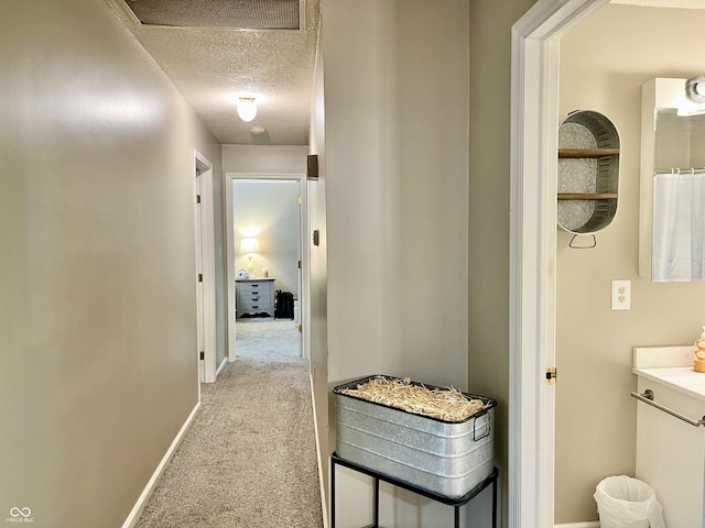 corridor featuring a textured ceiling, light carpet, and baseboards