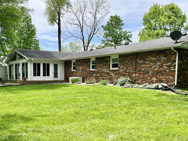 back of house with brick siding, a yard, and a sunroom