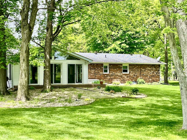 back of house featuring a yard, brick siding, and a shingled roof