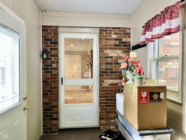 doorway with healthy amount of natural light, brick wall, and a textured ceiling