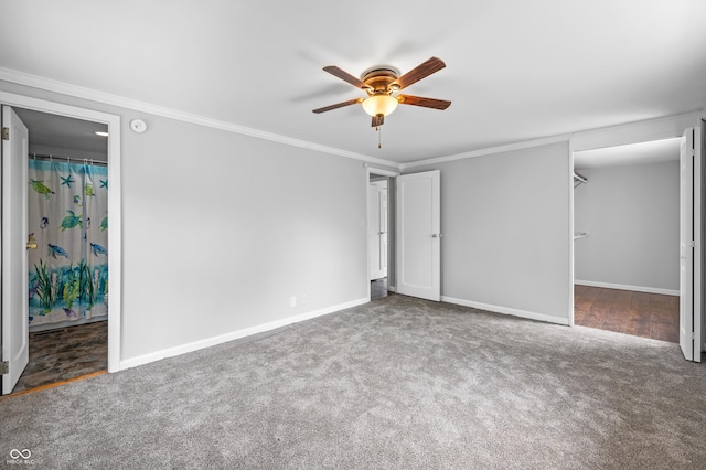 unfurnished bedroom featuring carpet, baseboards, a walk in closet, ornamental molding, and ceiling fan