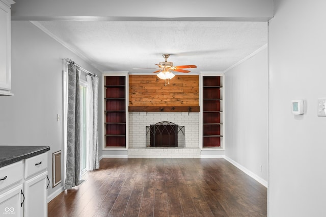 unfurnished living room with crown molding, dark wood-type flooring, ceiling fan, a brick fireplace, and a textured ceiling