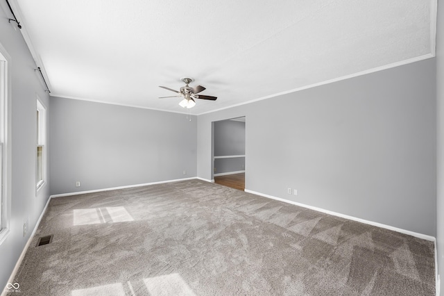 spare room with crown molding, carpet flooring, a ceiling fan, and baseboards