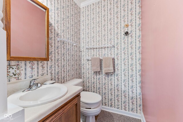 half bathroom with toilet, vanity, wallpapered walls, and baseboards