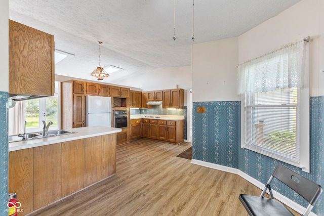 kitchen featuring freestanding refrigerator, oven, a sink, light wood-type flooring, and light countertops