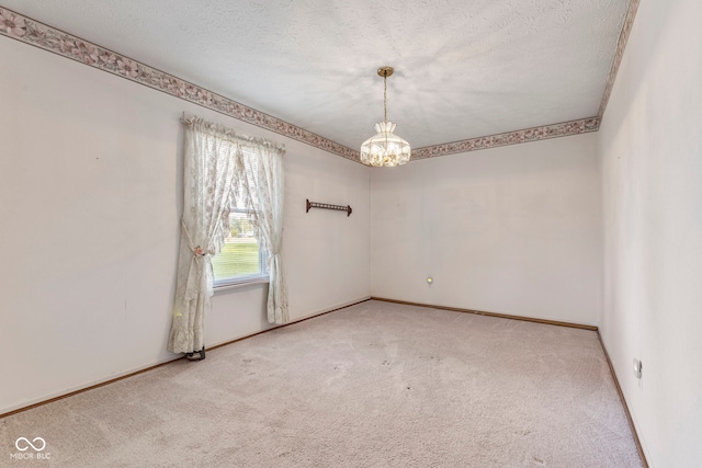 carpeted empty room featuring a chandelier, baseboards, and a textured ceiling