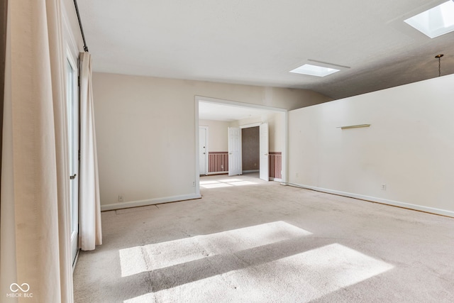 carpeted empty room with a skylight, vaulted ceiling, and baseboards
