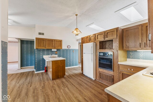 kitchen featuring black oven, freestanding refrigerator, a skylight, brown cabinetry, and wood finished floors