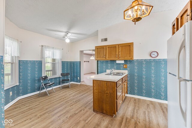 kitchen featuring freestanding refrigerator, a sink, brown cabinets, light wood-style floors, and a chandelier