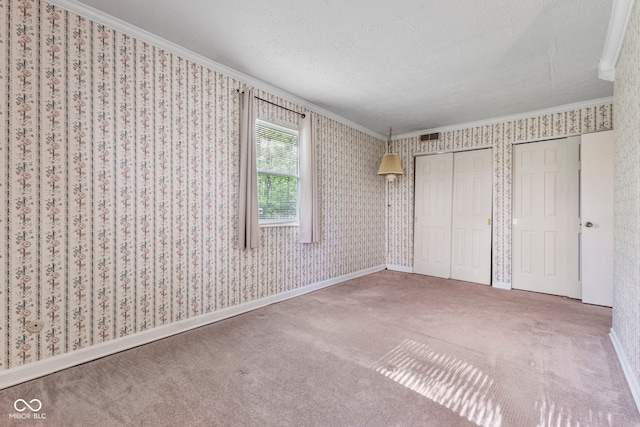 unfurnished bedroom with ornamental molding, multiple closets, carpet, a textured ceiling, and baseboards