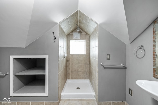 bathroom featuring vaulted ceiling, a tile shower, and a sink