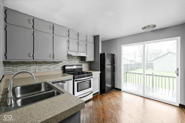 kitchen with appliances with stainless steel finishes, a sink, under cabinet range hood, backsplash, and dark wood-style flooring