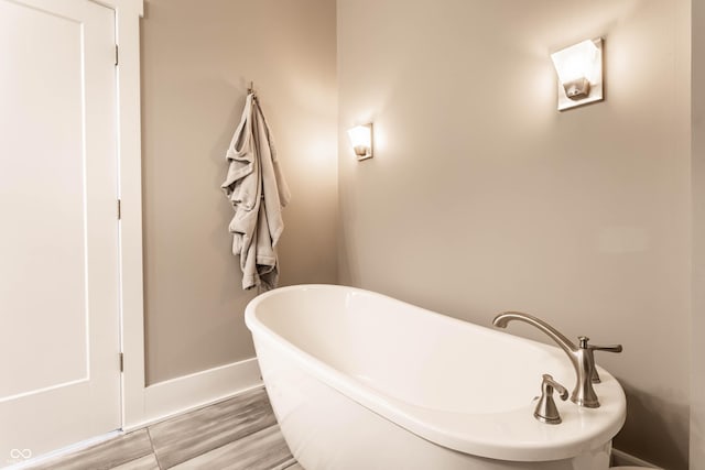 bathroom featuring a soaking tub, baseboards, and wood finished floors