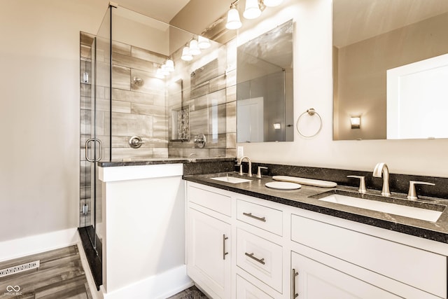 bathroom with a shower with door, double vanity, and wood finished floors