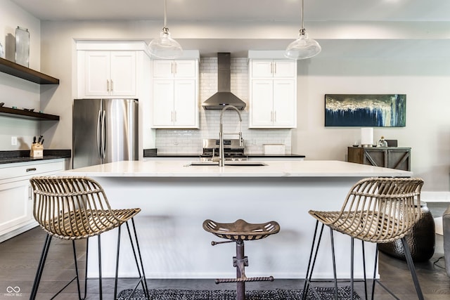kitchen featuring freestanding refrigerator, wall chimney exhaust hood, a breakfast bar area, open shelves, and tasteful backsplash