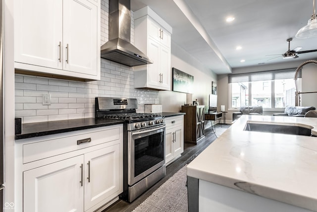 kitchen featuring gas range, wall chimney range hood, open floor plan, white cabinetry, and recessed lighting