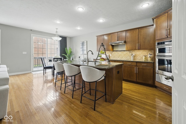 kitchen with a warming drawer, a kitchen bar, hardwood / wood-style floors, decorative backsplash, and an island with sink