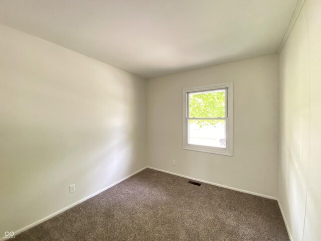 spare room featuring dark carpet and baseboards