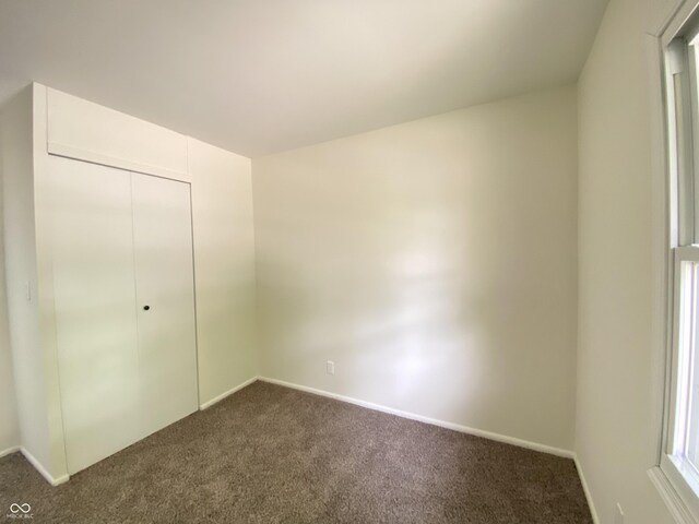 unfurnished bedroom with dark carpet, baseboards, and a closet