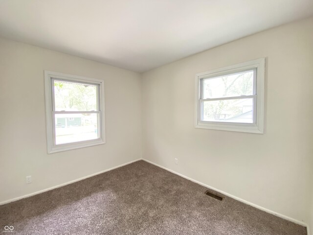 empty room with plenty of natural light, dark carpet, and baseboards