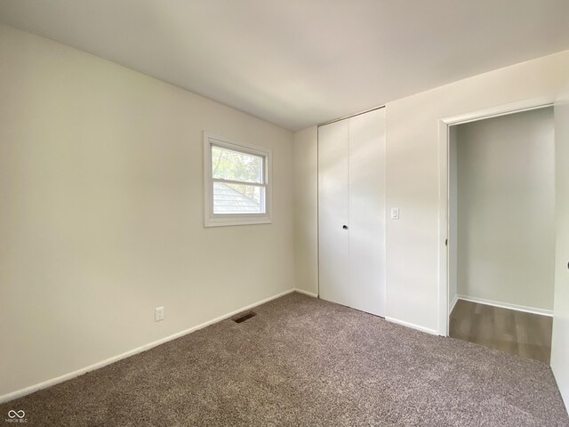 unfurnished bedroom featuring dark carpet, a closet, and baseboards
