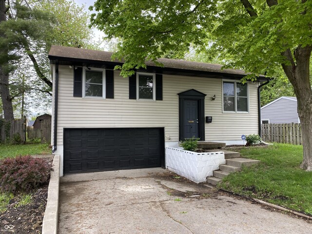 split foyer home featuring fence, concrete driveway, a garage, and a shingled roof