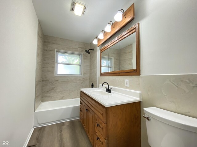 bathroom featuring wood finished floors, toilet, vanity, and tub / shower combination