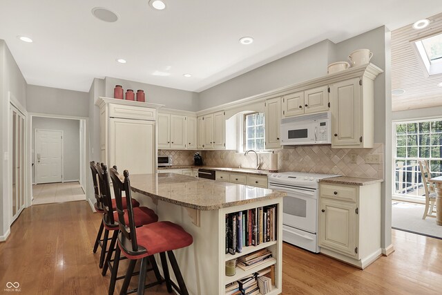 kitchen with white appliances, light stone countertops, a sink, a kitchen island, and plenty of natural light