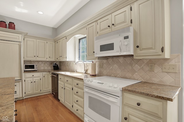 kitchen featuring white appliances, cream cabinets, a sink, backsplash, and light wood-style floors
