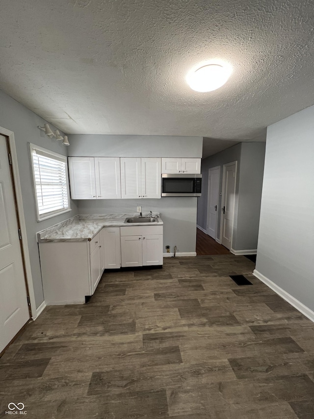 2037 Glenridge Dr, Indianapolis, IN 46218 - kitchen with stainless steel microwave, a textured ceiling, a sink, baseboards, and white cabinets