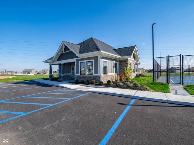 view of front of property with stone siding, uncovered parking, fence, a shingled roof, and board and batten siding