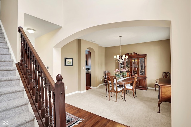 dining room with arched walkways, stairway, baseboards, a chandelier, and wood finished floors