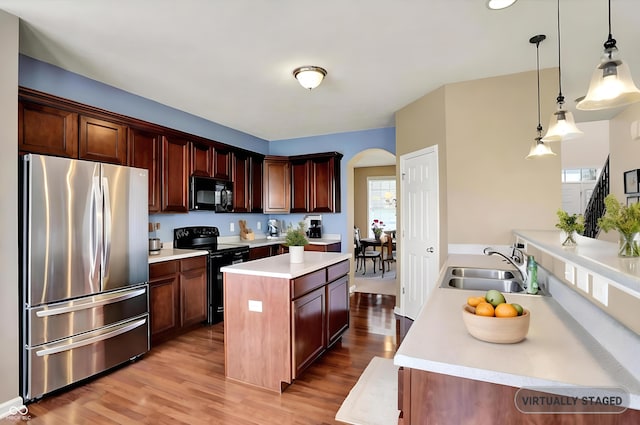 kitchen with black appliances, arched walkways, a sink, and light wood-style flooring