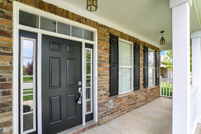 doorway to property with a porch and brick siding