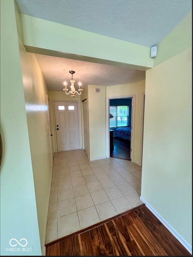 entryway with a chandelier, a textured ceiling, light tile patterned floors, and baseboards