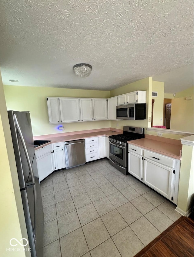 kitchen featuring stainless steel appliances, white cabinetry, light tile patterned flooring, a textured ceiling, and light countertops