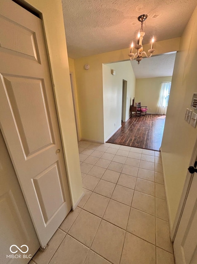 hallway with light tile patterned floors, a chandelier, a textured ceiling, and baseboards