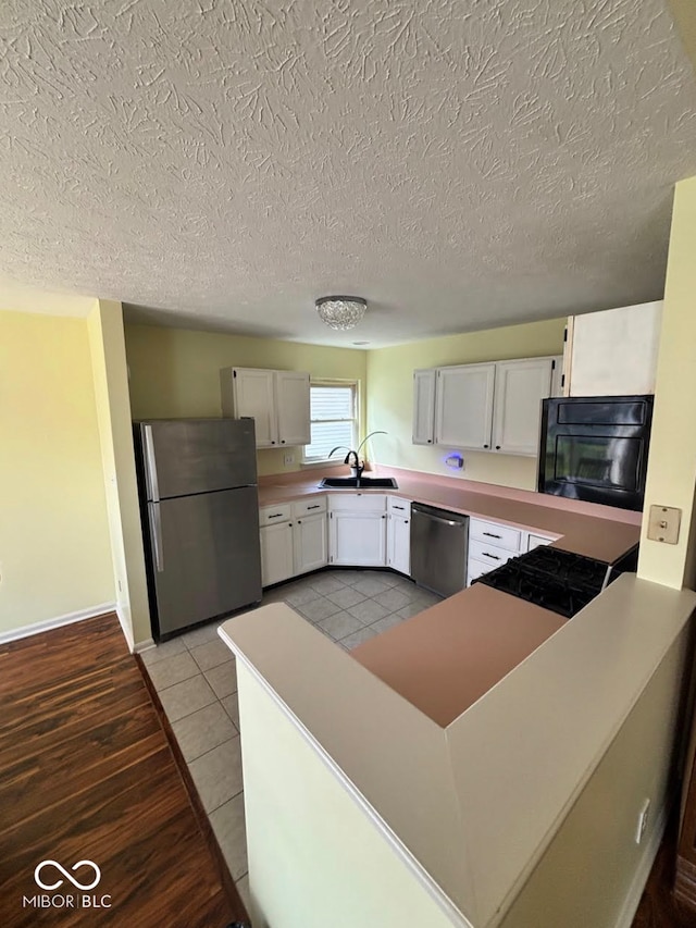 kitchen featuring stainless steel appliances, white cabinets, a peninsula, a textured ceiling, and a sink