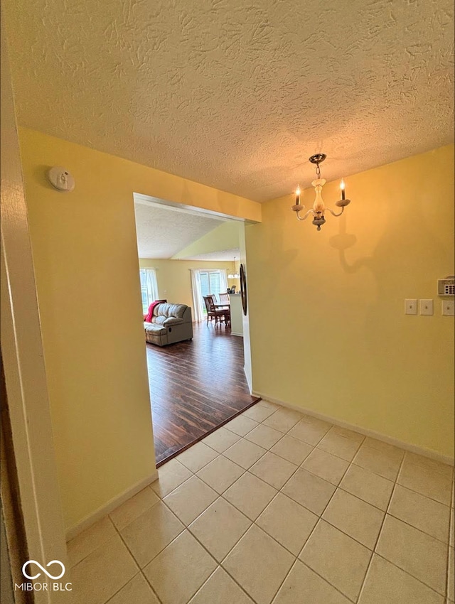hall with light tile patterned floors, a chandelier, baseboards, and a textured ceiling