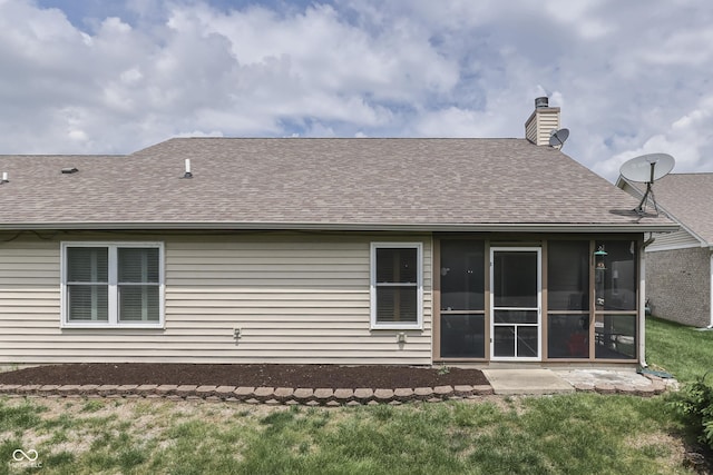 rear view of property with a shingled roof, a sunroom, a yard, and a chimney