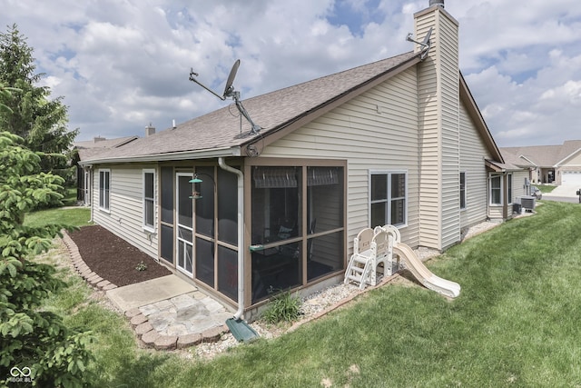 back of property with a chimney, a sunroom, a shingled roof, a yard, and central air condition unit