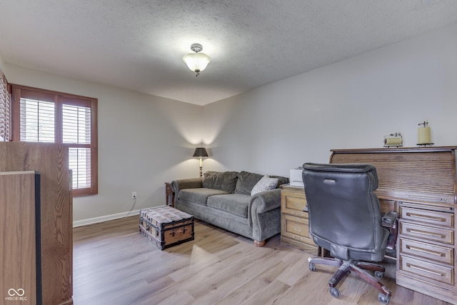 office space featuring light wood-type flooring, a textured ceiling, and baseboards