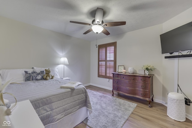 bedroom with light wood-style flooring, baseboards, a ceiling fan, and a textured ceiling