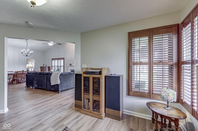 living room featuring light wood-type flooring, plenty of natural light, a chandelier, baseboards, and a textured ceiling
